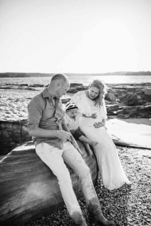 Maternity session - a little boy sits between his dad and pregnant mum on a beach