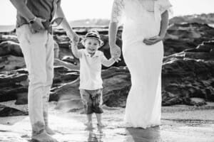 Maternity session - a little boy holds his parents hands, his mum holds her pregnant belly