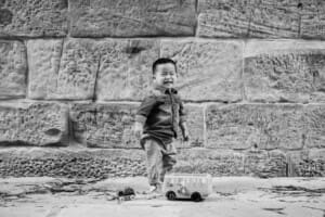 Family Session - A little boy stands against a stone wall and laughs