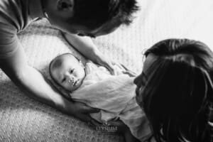 Newborn Session - parents hold their newborn baby, laying on a bed