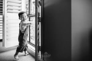 Newborn session - a little boy smiles, standing next to a bedroom window