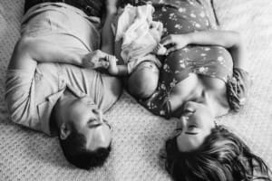 Newborn Session - parents lay on a bed, their newborn baby between them