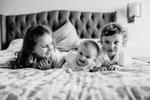 Family session - 3 children lay together on a bed and giggle