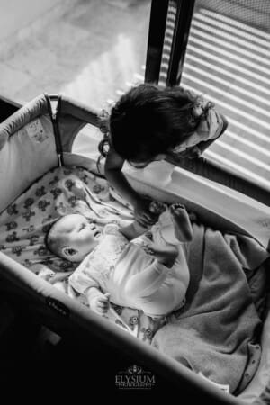 Family session - a boy leans over his baby sister's crib