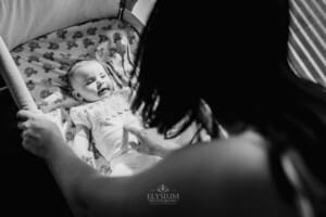 Family session - a mum leans over her baby's crib, chatting to her