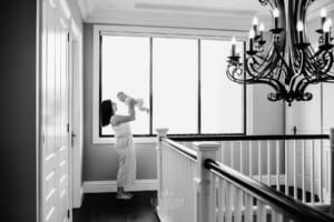 Family session - a mother lifts her baby above her, standing in a window