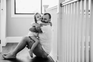Family session - a father hugs his little girl tightly as she sits with him