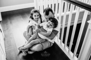 Family session - a dad sits with his kids in his lap hugging them