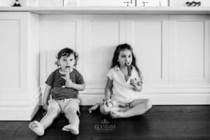 Family session - 2 children eat ice blocks, sitting under the kitchen bench