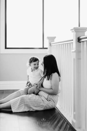 Family session - a mum sits with her son in her lap in front of a window
