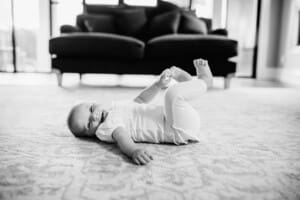 Family session - a baby rolls on the floor, grabbing her toes