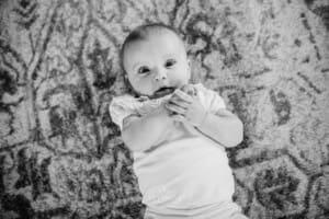 Family session - a baby laying on a carpeted floor, playing with her hands