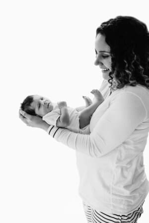 Newborn session - a mum stands in a bright window with her baby boy in her arms