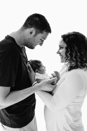 Newborn session - parents stand holding their baby between them smiling