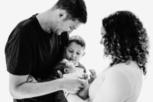 Newborn session - a family stand holding their new baby in front of a bright window