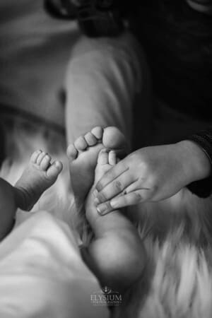 Newborn session - a little boy presses his foot against the baby's foot showing the size difference