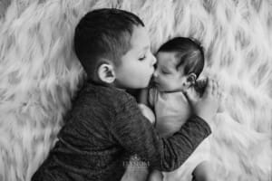 Newborn session - a little boy kisses his baby brother on the nose