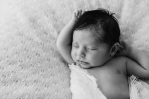 Newborn session - a baby sleeping on a white blanket with arms above his head