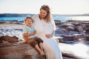Maternity session - a pregnant mum sits with her little boy on beach rocks