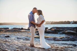 Maternity session - a couple hold the mums pregnant belly, standing on a beach