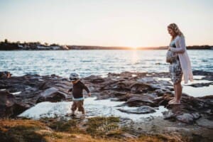 Maternity session - a little boy kicks water at the beach, his pregnant mum watching him