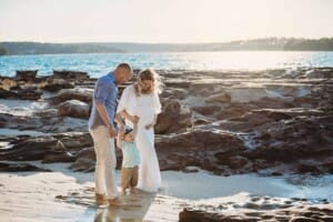Maternity session - a little boy holds his parents hands standing on a beach