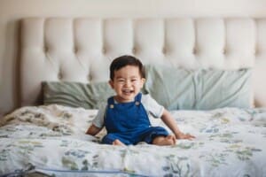 Newborn session - a little boy smiles while sitting on his parents bed
