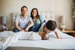 Newborn session - a family sitting on a bed, little boy kisses his baby brother