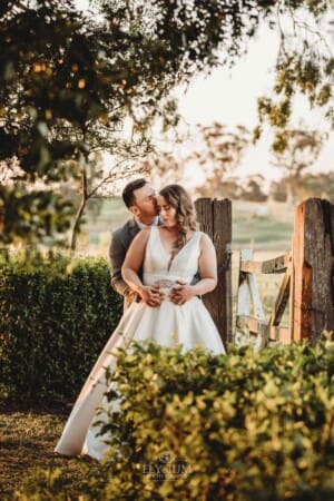 Gledswood Wedding - bride and groom stand cuddling against an old gate