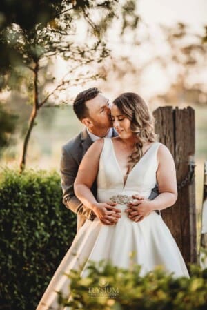 Gledswood Wedding - bride and groom stand cuddling against an old gate