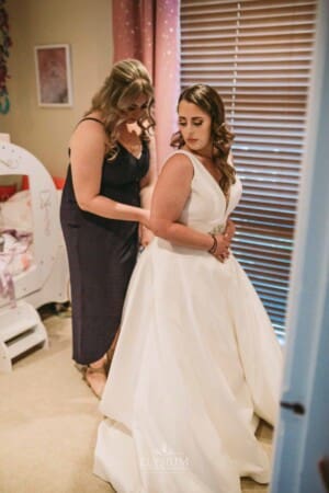 Gledswood Wedding - bridesmaid zips up the bridal gown