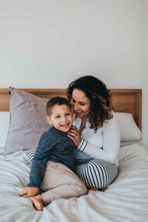 Newborn session - a mother cuddles her son in her lap sitting on a bed