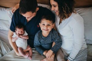 Newborn session - a family sit on a bed with their new baby