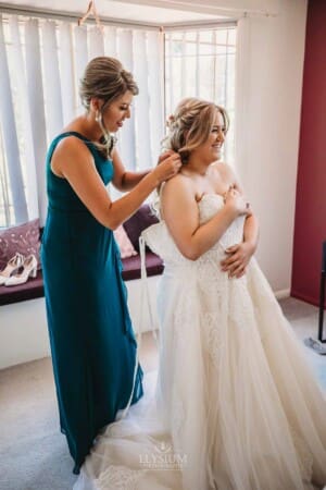 Gledswood Wedding Photo - Bridesmaid helps tie up the wedding gown