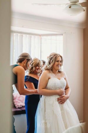 Gledswood Wedding Photo - Bridesmaids help tie the bridal gown