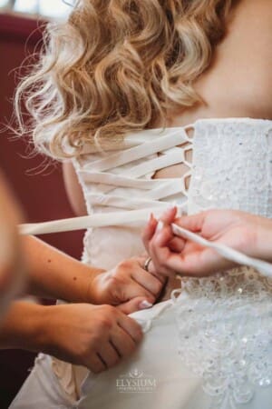 Gledswood Wedding Photo - Bridesmaids help tie the bridal gown