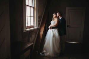 Gledswood Wedding Photo - groom kisses his bride standing at a window