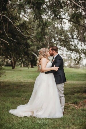 Gledswood Wedding Photo - groom kisses his bride as they stand in the homestead grounds
