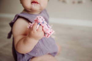 Cake Smash Session - baby girl sits with a handful of pink icing and cake