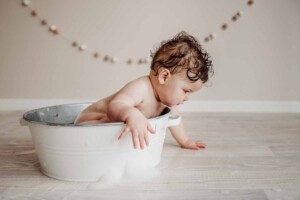Cake Smash Session - baby girl leans over a bath tub to look at bubbles