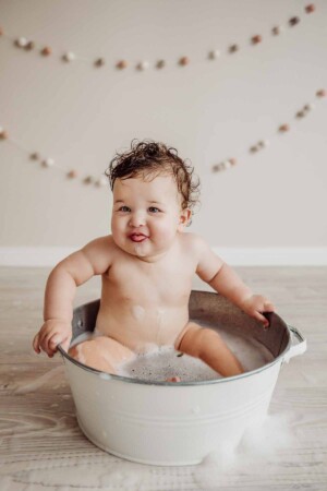 Cake Smash Session - baby girl blows raspberries as she sits in a bath tub