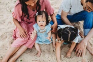 Family Photographer - parents sit in the sand with their little girls