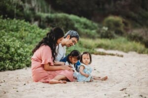 Family Photographer - parents sit on a sandy beach with their daughters