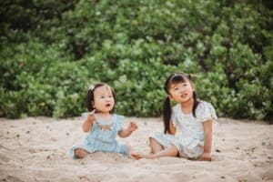 Family Photographer - little girls sit on a sandy beach together