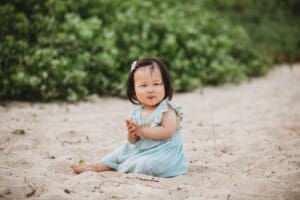 Family Photographer - a little girl brushes sand off her hands on a beach