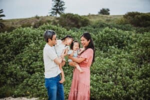 Family Photographer - parents hold their little girls standing on a beach