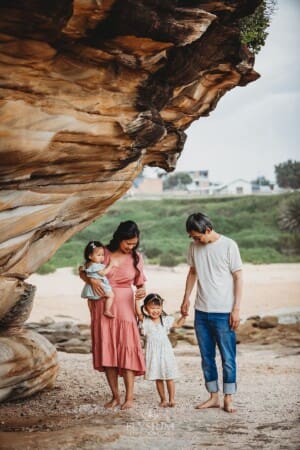 Family Photographer - parents hold their little girls hand as they stand on the beach