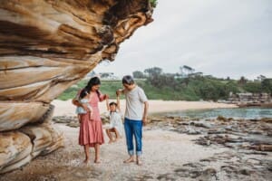 Family Photographer - parents swing their little girl between them as they stand on the beach