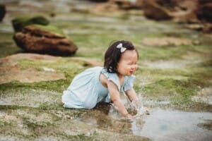 Family Photographer - a little girl splashes water in a beach rock pool