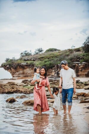 Family Photographer - parents walk with their little girls along a sandy beach